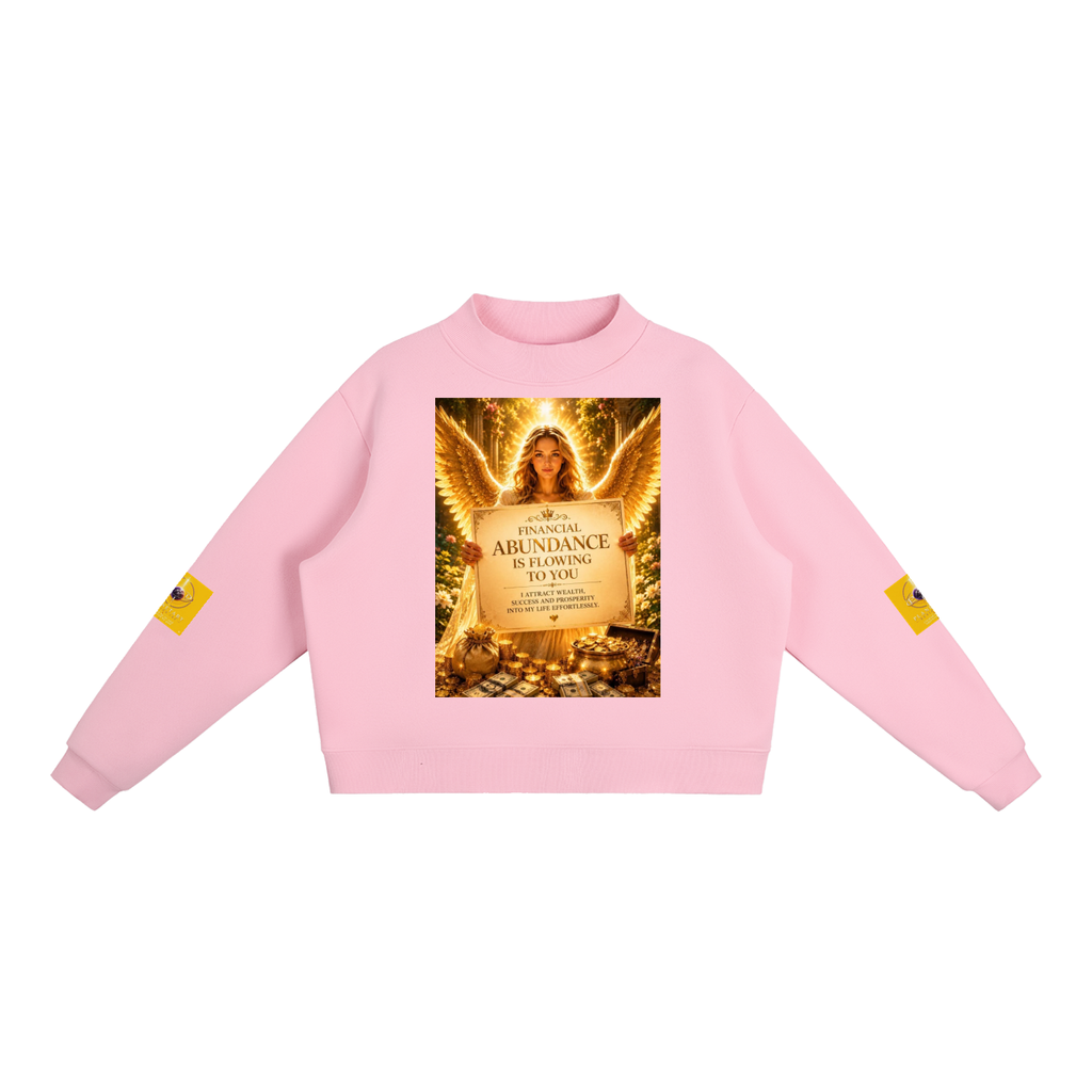 A light pink crewneck sweatshirt featuring a large graphic print on the front depicting an angel with wings and a sign that reads 'ABUNDANCE IS FLOWING TO YOU'. Each sleeve has a small yellow graphic patch, and the sweatshirt is displayed flat against a solid white background.