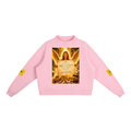 A light pink crewneck sweatshirt featuring a large graphic print on the front depicting an angel with wings and a sign that reads 'ABUNDANCE IS FLOWING TO YOU'. Each sleeve has a small yellow graphic patch, and the sweatshirt is displayed flat against a solid white background.