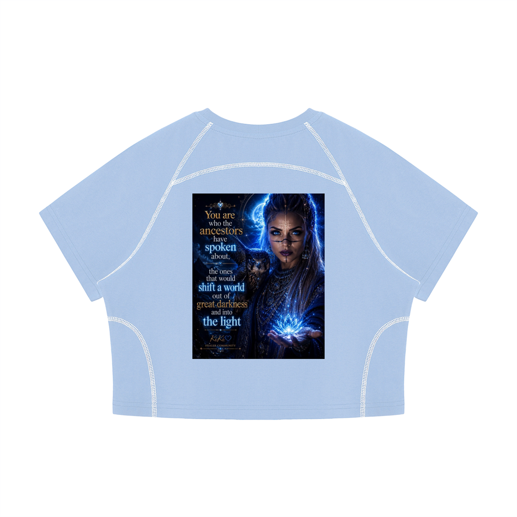 A light blue cropped short-sleeve t-shirt with white contrast stitching along the seams, featuring a large graphic print on the front depicting a woman with glowing blue energy and text.